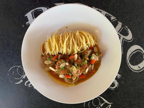 Spaghetti with braised meat, almonds, and green onions in a white bowl