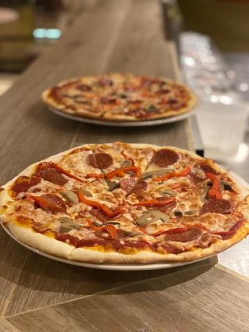 Two pizzas with pepperoni, sausage, bell peppers, and mushrooms on a table.