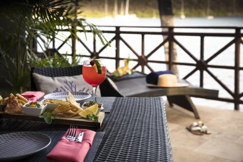 Outdoor dining by water with cocktail and appetizers on table.