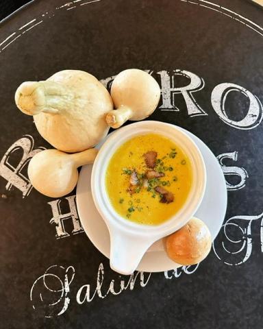 Creamy soup garnished with herbs and croutons beside round bread rolls on dark surface
