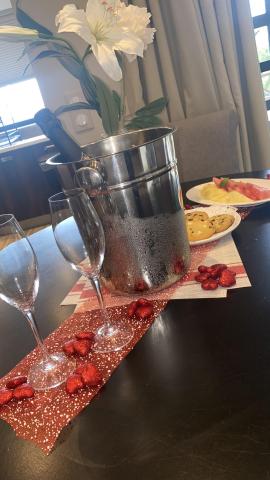 Romantic table setup with champagne, flutes, fruits, cookies, and floral decor.