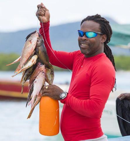 Man in sunglasses and red shirt happily showing fish caught on boat trip