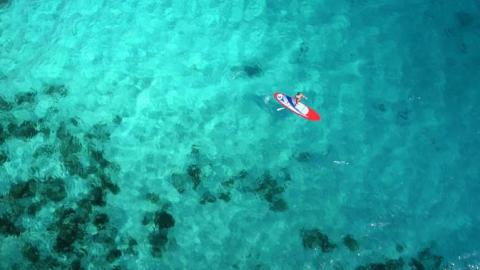 Aerial view of person on red paddleboard in clear turquoise sea