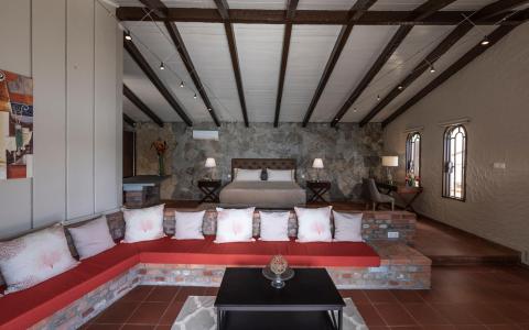 Rustic cozy bedroom with tufted bed, wooden beams, and vibrant cushions.