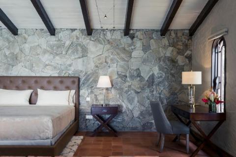 Stylish modern bedroom with rustic stone wall, wooden beams, and terracotta floor tiles.