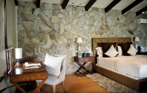 Stylish bedroom with plush headboard, stone wall, and cozy chair.