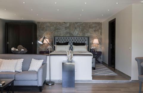 Stylish modern bedroom with stone wall, tufted headboard, and cozy gray sofa.