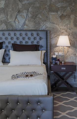Stylish bedroom with dark gray tufted headboard, white sheets, and rustic stone wall.
