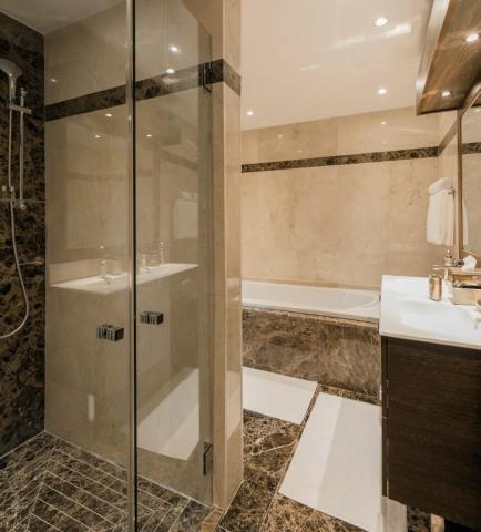 Luxurious modern bathroom with glass shower and beige stone tiles