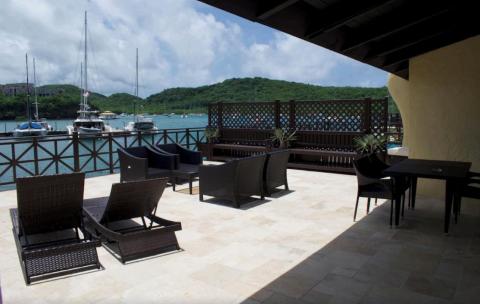 Luxurious waterfront deck with wicker furniture overlooking a harbor with sailboats
