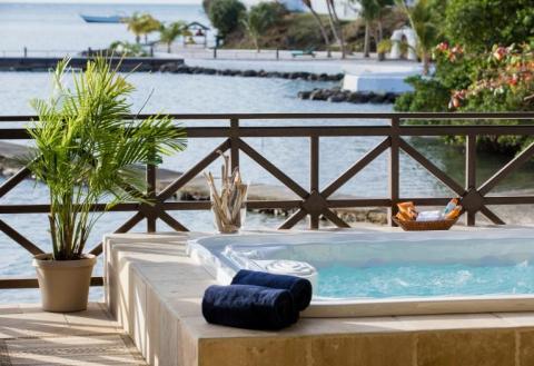 Outdoor jacuzzi on balcony overlooking bay with boats and greenery, towels and plant decor.