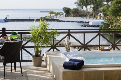 Outdoor spa and dining area overlooking a serene bay with a boat and palm trees.