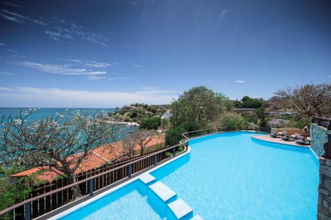 Infinity pool overlooking sea with lounge chairs and clear sky