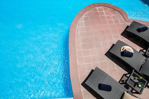 Swimming pool with heart design, loungers, sun hat and drinks on a sunny day