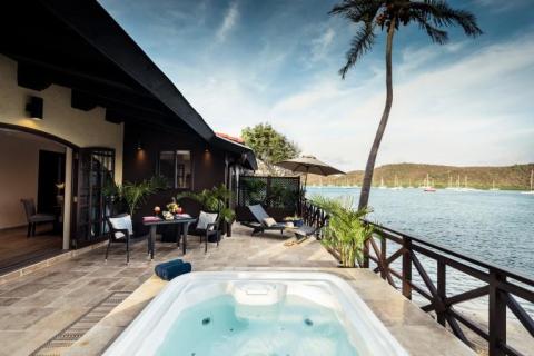 Luxurious outdoor jacuzzi and dining area by a lake with boats and a palm tree