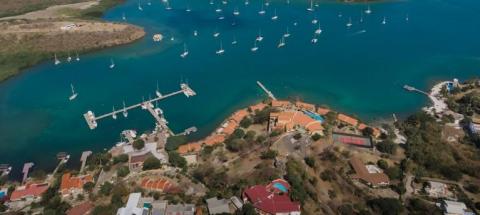 Aerial view of coastal marina with moored sailboats, buildings, and green spaces