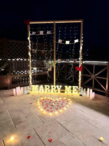 Romantic outdoor marriage proposal setup at night with lights and rose petals.