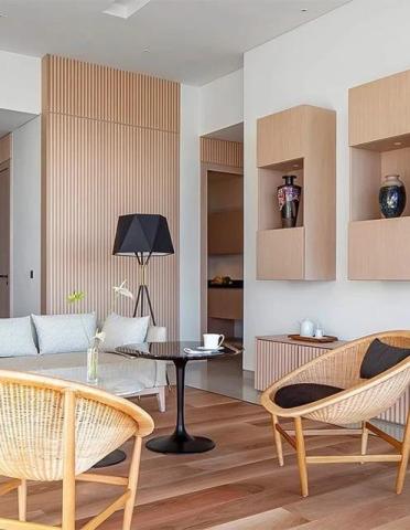 Modern living room with light wood panels, rattan chairs, and white sofa.