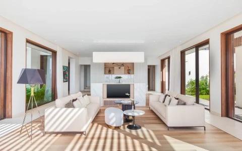 Modern living room with natural light, white sofas, fireplace, and flat screen TV.