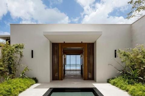 Modern house entrance with wooden doors, lush plants, and ocean view