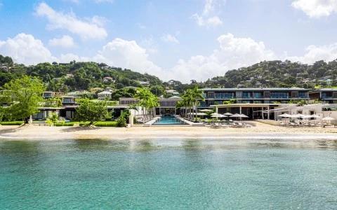 Luxurious beachfront resort with pool, modern buildings, and lush hills