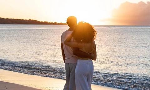 Couple embracing at sunset on beach, warm hues, calm sea background