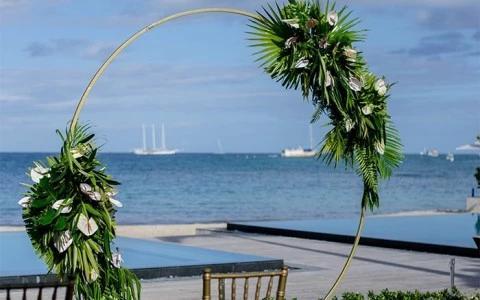Outdoor beach wedding setup with floral rings, pool, and sailboats.