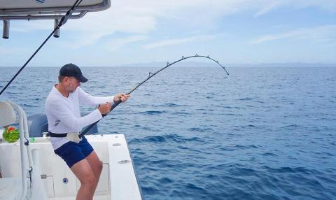 Man fishing in ocean on boat, holding bending rod, under cloudy sky, calm sea.