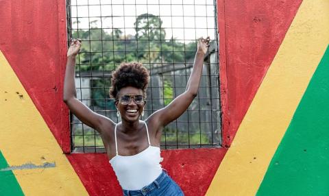 Joyful woman with afro smiling at colorful wall outdoors, happy mood captured in daylight.