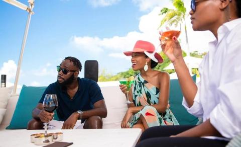 Three friends enjoy drinks outdoors on a sofa under blue sky