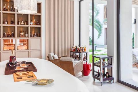 Modern indoor bar with whisky set, wooden cabinets, and garden view through sliding doors.