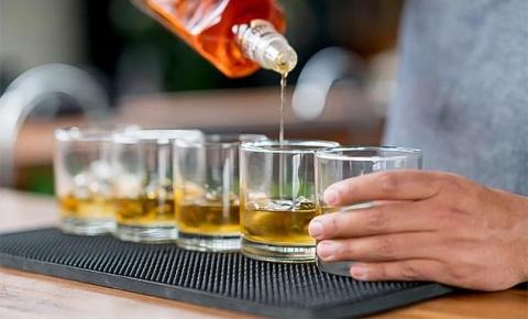 Person pouring whiskey into glasses on black mat, close-up shot