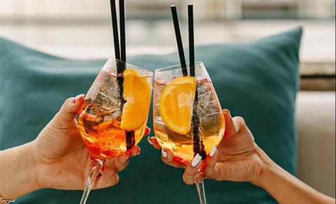 Hands toasting with orange drinks garnished with slices, festive mood.