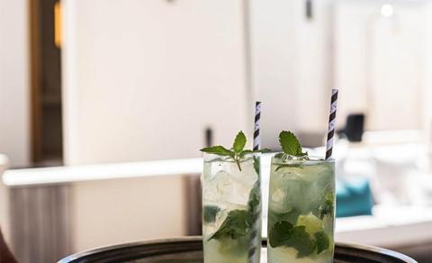 Two mojito drinks with mint garnish and straws in a cozy indoor setting
