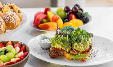 Colorful brunch spread with avocado sandwich, fresh fruit, and pastries