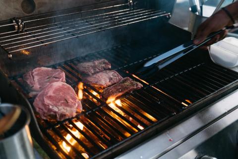 Person grilling seasoned beef on an outdoor BBQ with visible flames