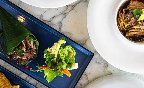 Elegant Asian salads and noodle dish with meat garnished with herbs and flowers on marble