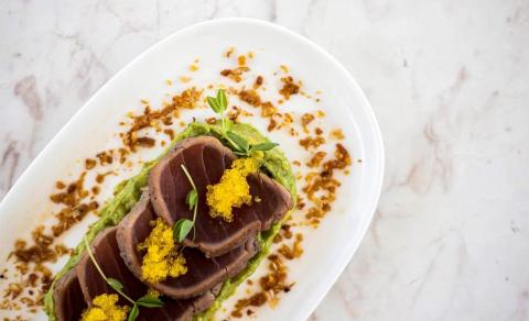 Seared tuna on guacamole with yellow roe and crispy crumbs on a white plate