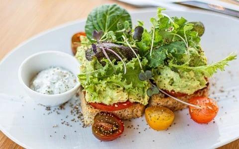 Avocado toast with tomato slices, salad greens, and herb dressing on a plate