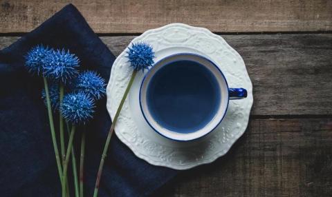 Blue thistle flowers and white cup with tea on wooden table, rustic aesthetic.