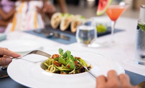 Outdoor dining table with pasta dish, drinks, and people enjoying a meal.