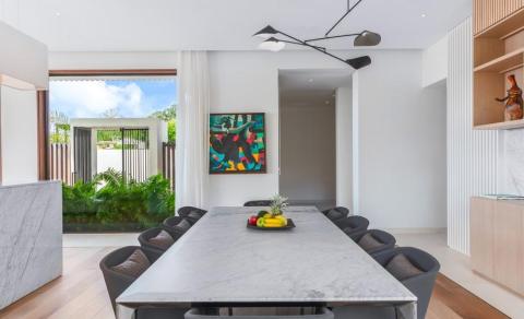 Modern dining room with marble table, lush courtyard view, and vibrant art.