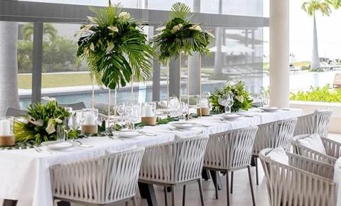 Outdoor dining setup by tranquil water with lush greenery and modern architecture.