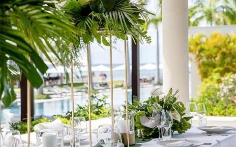 Elegant outdoor dining setup with marina view, lush greenery, and floral decor