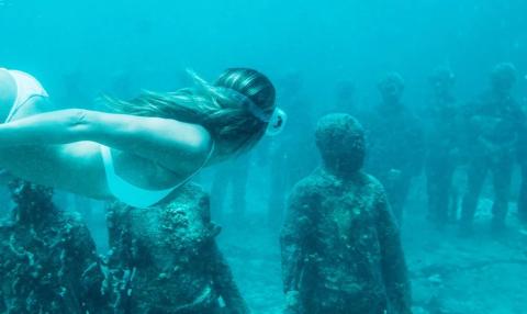 Diver explores eerie underwater statue garden in clear blue-green waters