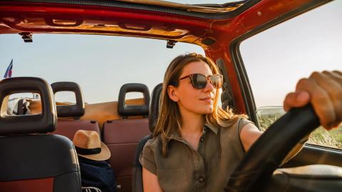 Relaxed woman driving red convertible in sun with sunglasses and straw hat