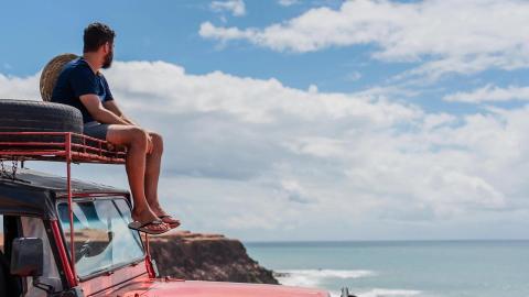 Man on red off-road vehicle overlooking sea from clifftop, tranquil scene