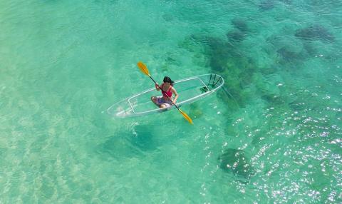 Person kayaking in turquoise water with transparent kayak and yellow oar