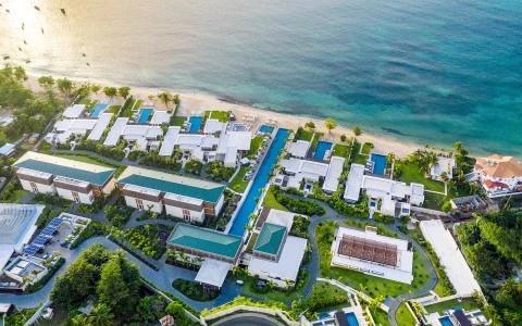 Aerial view of a seaside resort with white buildings, pools, and a sandy beach