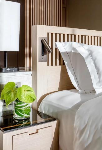 Modern bedroom with white linens, wooden headboard, and marble-topped bedside table.